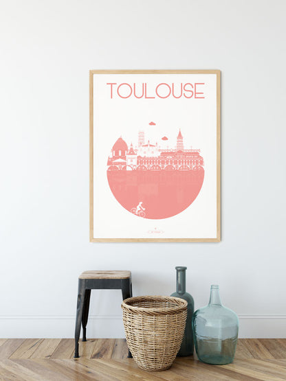 Affiche "Toulouse – La Ville" en rose accrochée au mur, accompagnée d'une plante verte et d'une table basse.